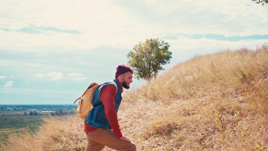 Side view of tourist with backpack climbing up on hill