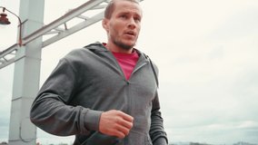Runner stopping with shortness of breath on bridge with cloudy sky on background