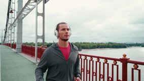Sportsman with headphones jogging on bridge with nature landscape on background