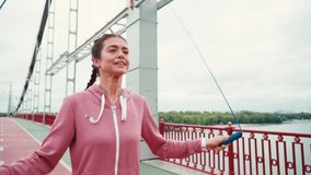Smiling sportswoman rope jumping on bridge with nature landscape on background