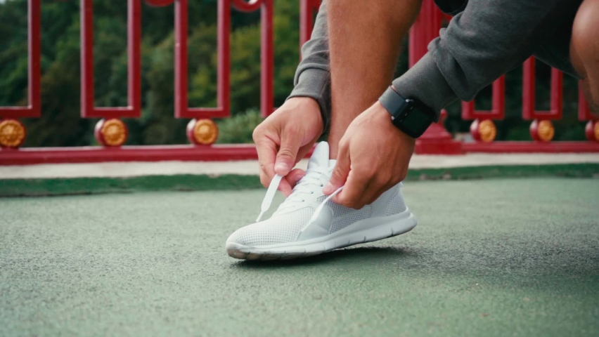 Cropped view of sportsman with smartwatch tying laces of sneaker on bridge