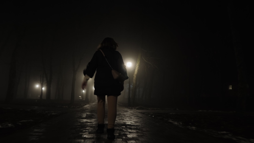 Scared young woman looking back runs away from someone at night in city park Royalty-Free Stock Footage #1067518574