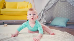 baby boy looking at camera while crawling on blanket near sofa and tent