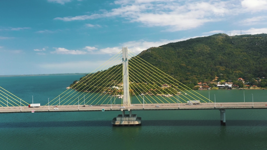 Drone aerial side panning view of concrete cable-stayed bridge traffic above turquoise color ocean
