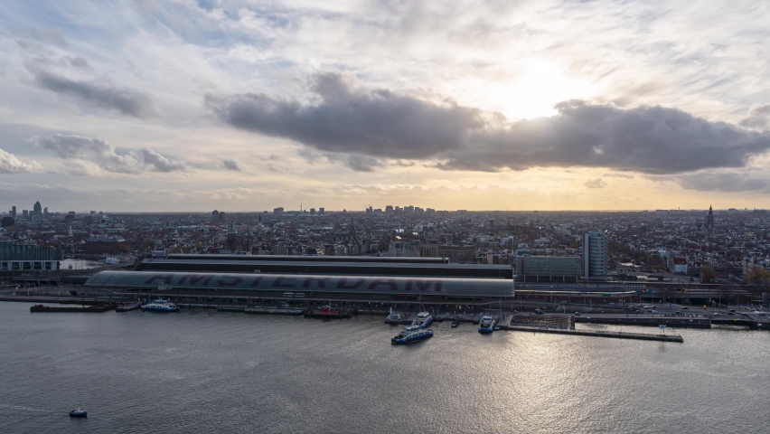 4k time lapse of sunset over Amsterdam city center with the central train station and the IJ river with trains, busses and ferries transporting commuters 