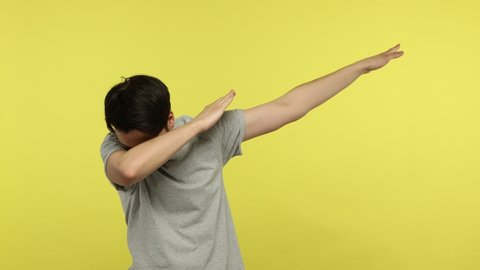 Positive carefree young man showing dab dance pose, triumph gesture, expressing joy and happiness, celebrating with internet meme, dabbing trends. Indoor studio shot isolated on yellow background