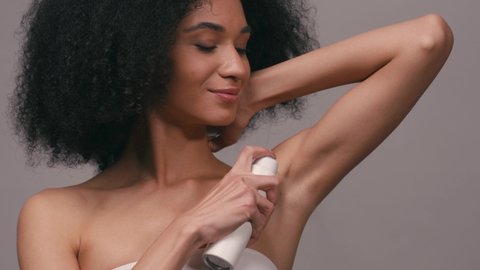positive african american woman applying deodorant isolated on grey