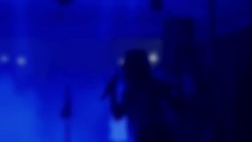 Rear view of a girl singing to microphone on blurred background. Unrecognisable person pop singer on concert night party club. Party concept, have fun tonight. Slow motion video.