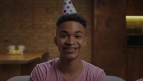 Young adult African American man wearing birthday hat singing happy birthday song at camera. Webcam view of man congratulating someone online.