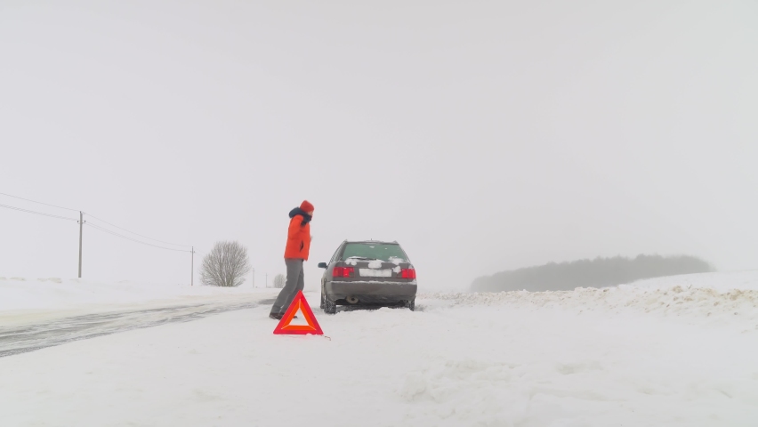 The car is parked on the side of the road on an empty road. It is worth a sign of attention or an emergency stop. Winter snowfall. The man screams and recoils in anger. Crazy.