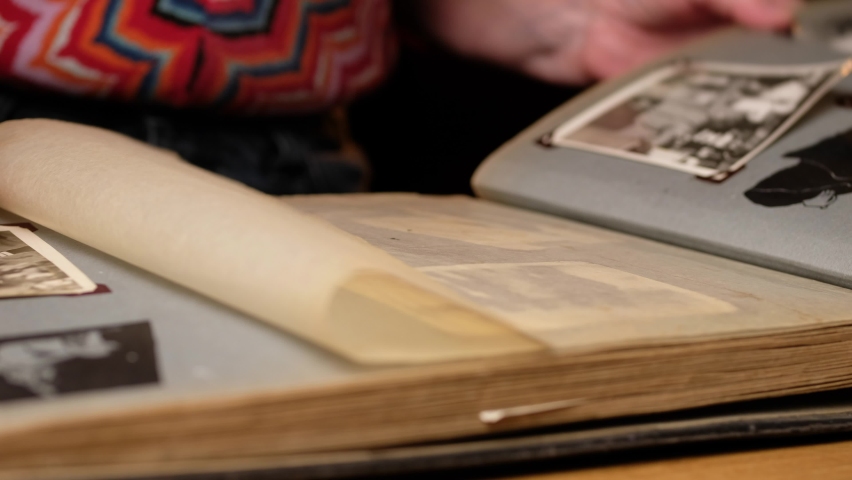 Elderly woman looks through an family album with old photos at table at home. Old granny memories past times and remembering his life.