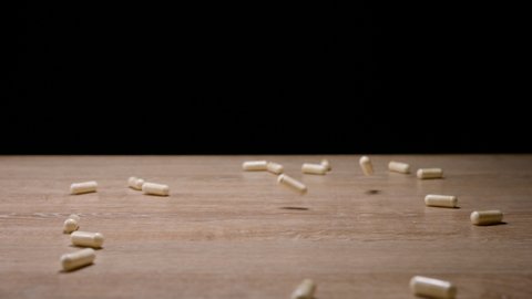 Medical capsules falling down wooden table on black background