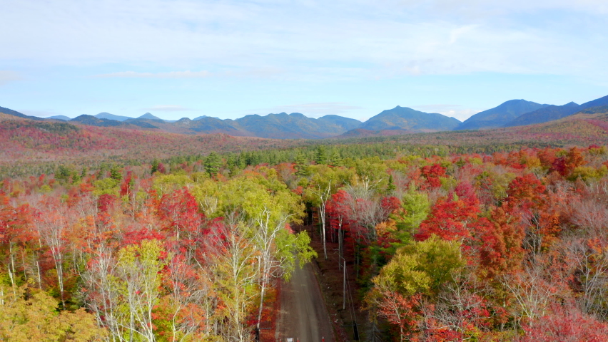 Stunning Rising Aerial View of a Valley and Mountain Ridge Covered in Vibrant Autumn Foliage, Bright Red and Yellow Leaves, Drone Footage of the Adirondacks, New York