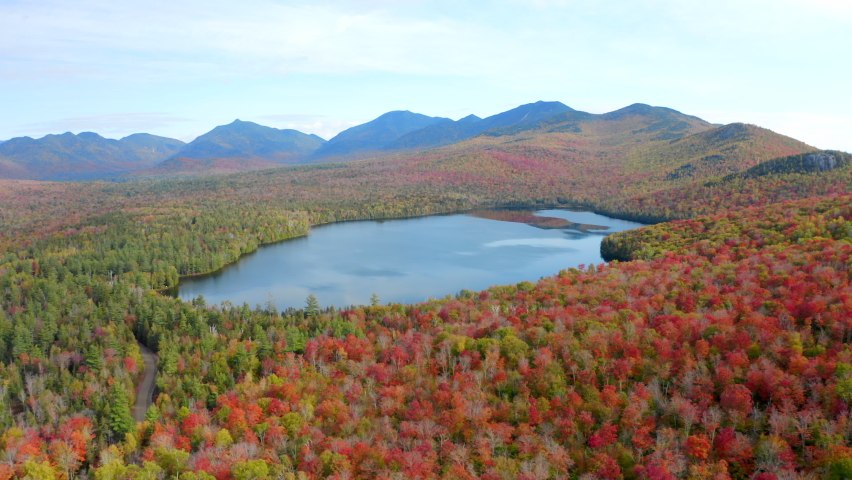 Aerial View of a Lake Surrounded by Beautiful Fall Colors with the High Peaks of the Adirondack Mountains in the Background, Forward Drone Movement
