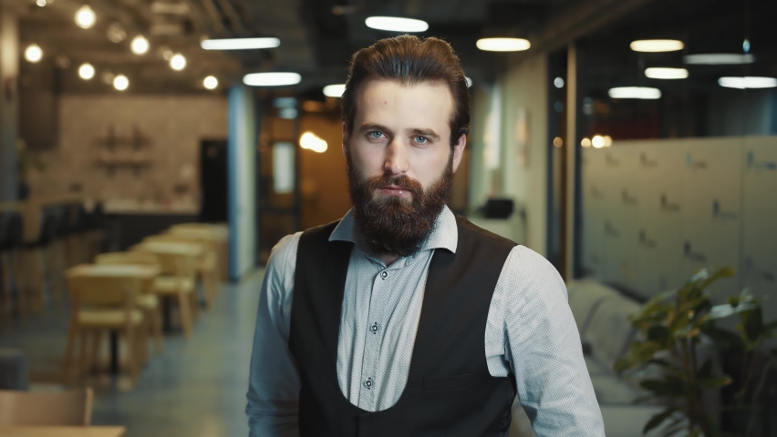 Close up portrait of a successful businessman with a beard of Caucasian appearance. The man folds his arms and looks intently at the camera. The look of a confident businessman leader.
