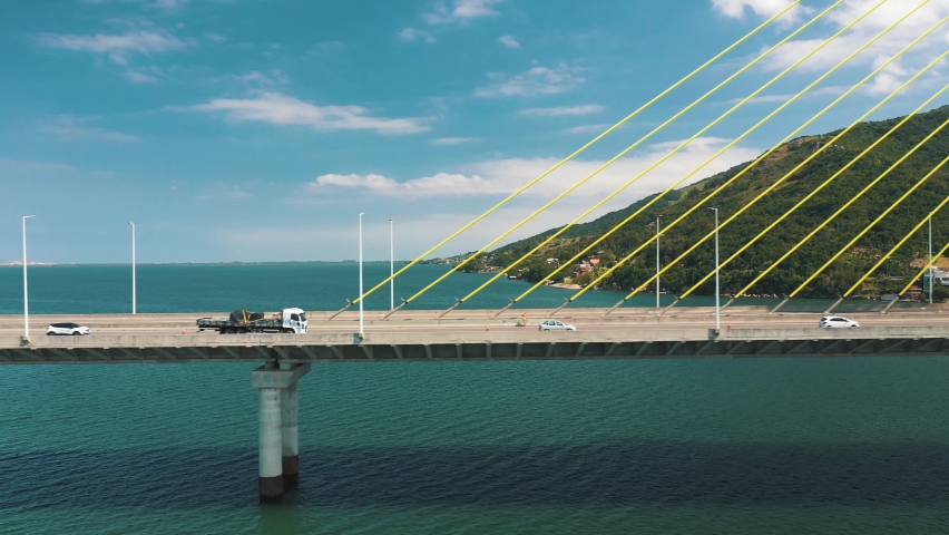 Drone aerial side panning view of concrete cable-stayed bridge traffic above turquoise color ocean
