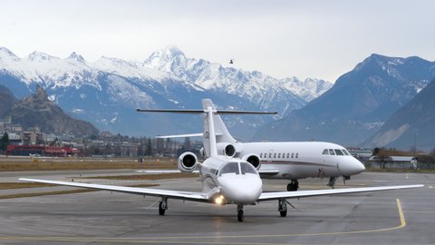 Sion , Switzerland - 12 20 2020: Cessna private jet taxiing at Sion Airport as helicopter flies over the alps