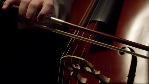 Artist plays with a bow on the strings of the cello in the darkness. Close-up musician plays with a bow of a violoncello.