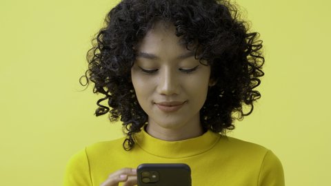 Young beautiful woman using smartphone at yellow background. She looking to smartphone with smiling.