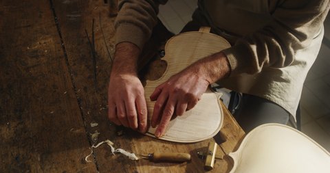 Cinematic shot of master artisan luthier working on creation of handmade fine quality wood violin in his creative workshop. Concept of spiritual instrument, handmade, art, orchestra, artisan, music.