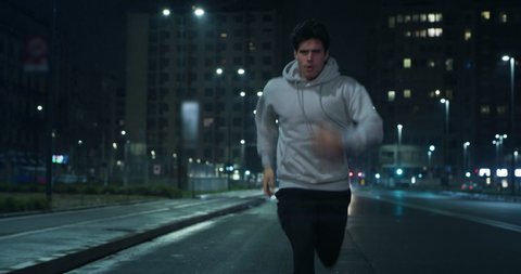 Cinematic shot of young male sportsman with athletic body is running with effort and dedication in city center with snow falling at night. Concept of determination, motivation and goal achievement.