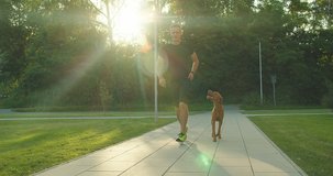Silhouettes of runner and dog on city street under sunrise sky in morning time. Outdoor walking. Athletic young man jogging, working out with his dog are running in town. 4K video SLOW MOTION
