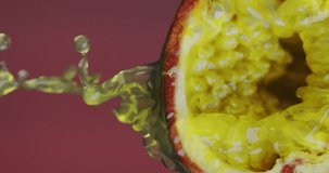 Vertical Video. Juice splashing flow down from natural passion fruit on pink studio backdrop with copy space