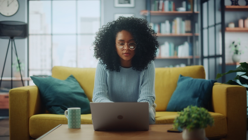 Portrait of a Beautiful Authentic Latina Female in a Stylish Cozy Living Room Using Laptop Computer at Home. She's Browsing the Internet and Checking Videos on Social Networks and Having Fun. Royalty-Free Stock Footage #1067577188