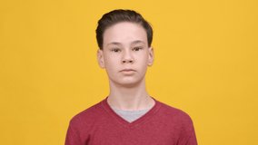 Confident Teen Boy Touching Hair Posing Smiling To Camera Standing Over Yellow Studio Background. Teenager's Haircare. Self-Confidence In Teenage Age Concept. Slow Motion