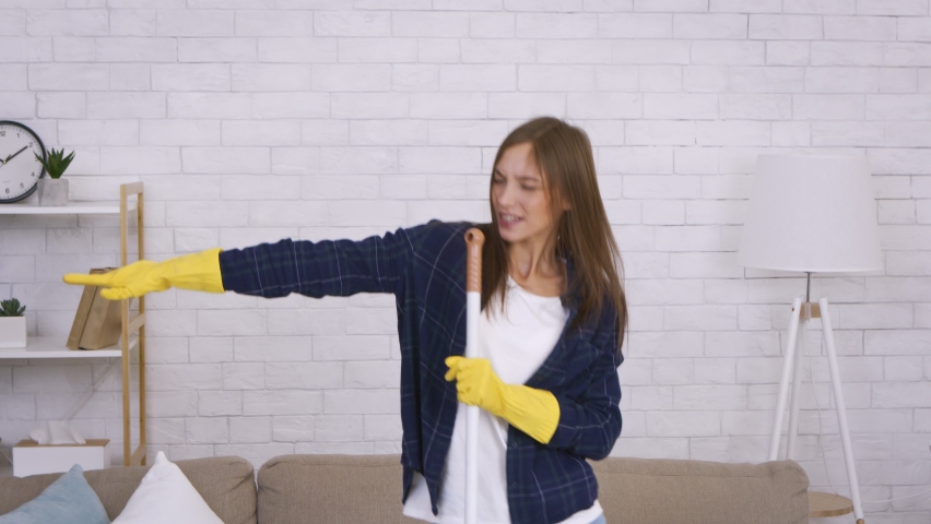 Emotional young woman singing into mop, having fun during home cleaning, feeling like a popular rockstar with guitar, slow motion Royalty-Free Stock Footage #1067579159
