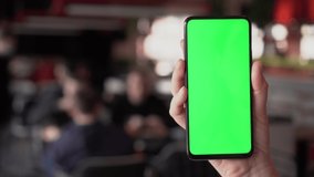 Close up of a woman's hand holding a mobile telephone with a vertical green screen in restaurant chroma key smartphone technology cell phone street touch message display hand.