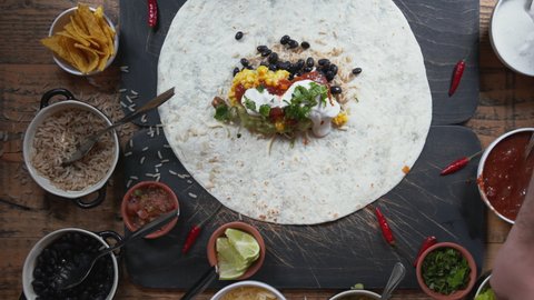 Making a traditional Mexican cuisine dish burrito on the table. Top down view of food preparation on the table. Wrapping up and cutting burrito in half