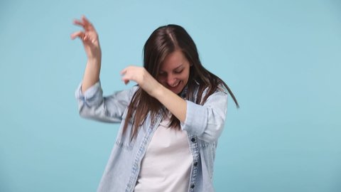 Slow motion fancy vivid bright beautiful long hair young woman 30s years old in denim jacket white t-shirt dance fool around having fun gesticulate with hands isolated on pastel blue background studio