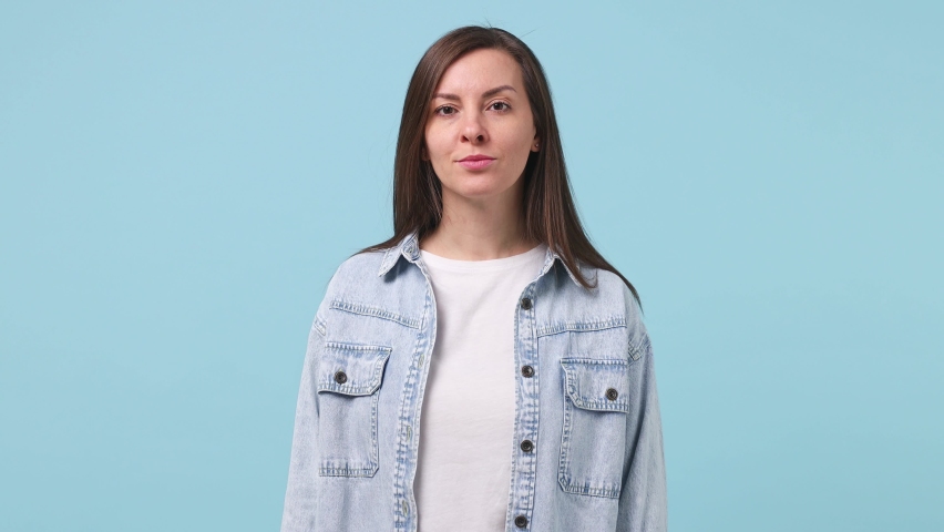 Beautiful long hair brunette young woman 30s years old in denim jacket white t-shirt isolated on pastel blue background studio. People lifestyle concept. Looking camera charming smile wink eye blink