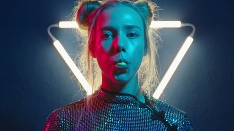 Girl with bubble gum. Camera zoom. Young woman looking at the camera in the neon light of the club . Portrait of a beautiful futuristic lady close-up. 