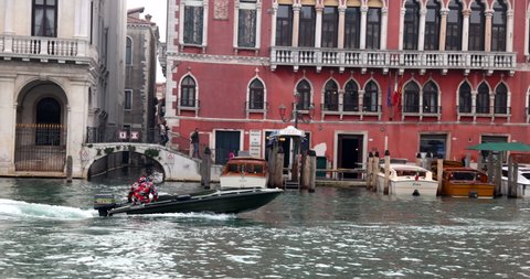 Venice, Italy - 18.11.2020: Young man steering motorboat speedboat fast on grand canal near rialto water bus stop and moored boats slow motion 
