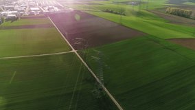 Drone view of electric supports against the sky among empty green and grey fields. The civilization is visable on the background. Sunny day, summer, countryside, high voltage line. 4K video.