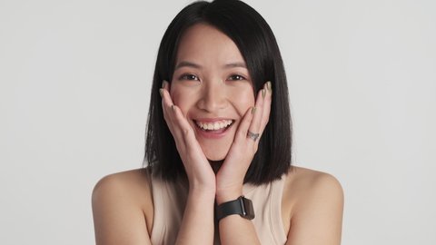 Beautiful amazed Asian girl rejoicing because of good news on camera over white background. Wow expression