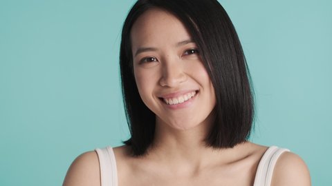 Beautiful Asian girl showing on camera fresh clean face looking happy isolated on blue background
