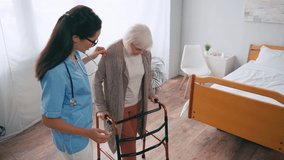 senior woman stepping with walkers near gesturing nurse