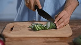 cropped view of man cutting fresh cucumber on chopping board