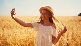 joyful girl in white dress and straw hat taking selfie in wheat field