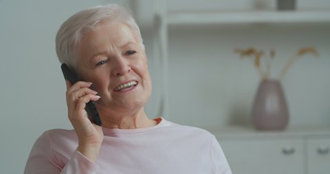 Happy middle aged senior caucasian woman grandma relaxing on cozy sofa talking on smartphone with children and grandchildren remotely. Close-up female face elderly lady sharing news on mobile phone
