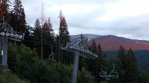 Still ski lift at sunset. Peaceful scenic landscape with mountain peaks in red sunlight. Tranquil ski resort wilderness view in summer during lockdown. Untouched forest wilderness, dark trees and sun