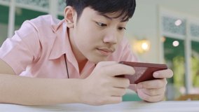 Asian high school boy is playing online game on his mobile phone . Hand held, slow motion.