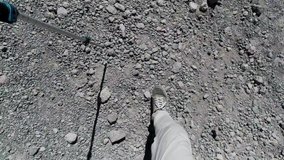 Feet in boots of hiker slipping on the rocky descent from the mountain. Clip. First person top view of one climber walking forward with a pole.