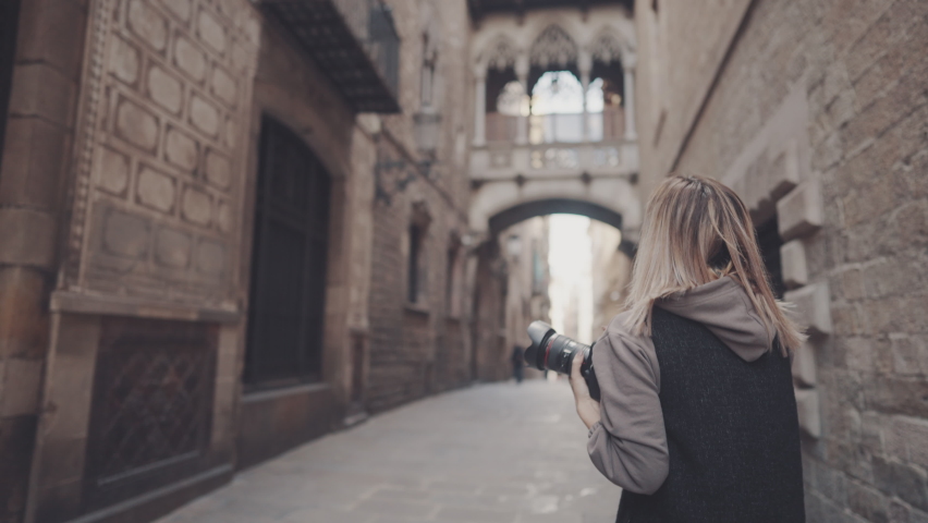 Beautiful Female tourist with dslr photo camera walking through old town narrow streets, Barcelona, Spain. She takes photos. Prores 10 bit color space