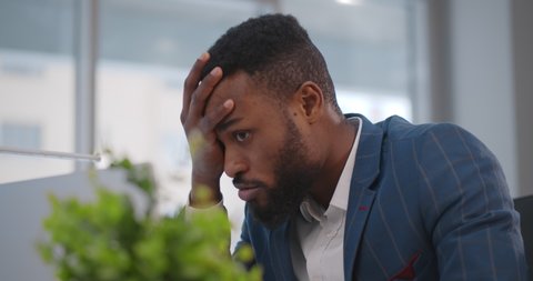 Close up of stressed and upset african man with laptop working at office. Portrait of afro-americna businessman receiving email with bad news feeling frustrated sitting at desktop in office