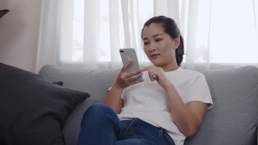 Young Asian woman using a smartphone for shopping online by application E-commerce is easy to sell or buy everything sitting on the sofa in the living room at home | Shutterstock HD Video #1067619494