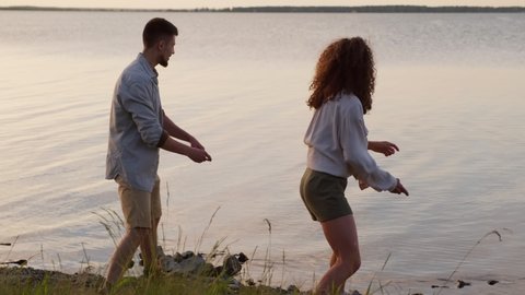 Rear view shot footage of active young couple having fun skipping pebbles on lake water surface in evening